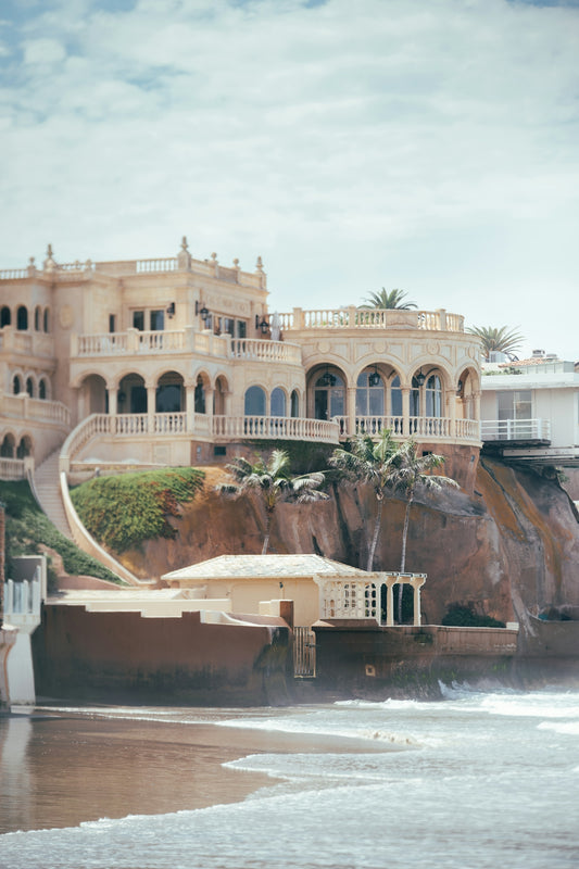 Ornate mansion on a cliff above a beach with waves.